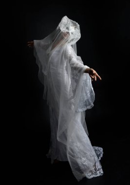 Full length portrait of beautiful woman wearing  white bridal fantasy  gown with butterfly mask and ethereal veil.  Dancing with gestural arm poses, isolated on black studio background.