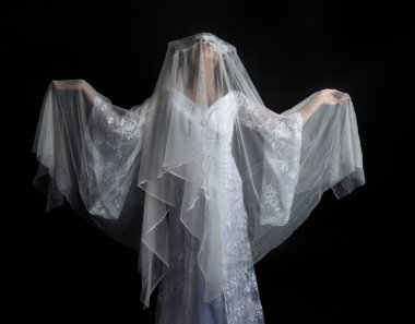 close up portrait of beautiful woman wearing  white bridal fantasy  gown with butterfly mask and ethereal veil.  Dancing with gestural arm poses, isolated on black studio background.