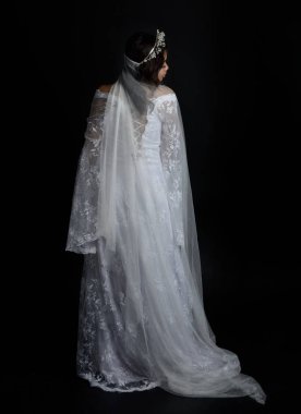 Full length portrait of beautiful woman wearing  white bridal fantasy  gown with butterfly mask and ethereal veil.  Dancing with gestural arm poses, isolated on black studio background.