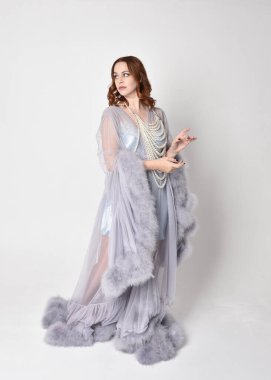 Portrait of beautiful red haired woman wearing glamorous  fluffy bridal dressing gown and vintage pearl necklace.  Elegantly standing pose, isolated on white studio background.