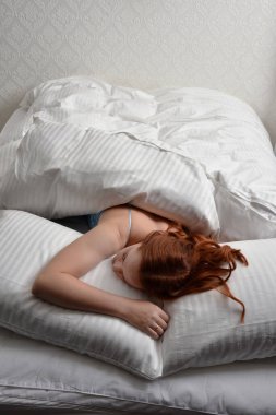 Portrait of beautiful red haired woman wearing comfortable pyjamas, casualy resting in bed, getting ready for sleep,  in a glamorous white bedroom location background.