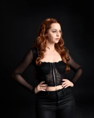 close up portrait of beautiful woman with long red hair wearing sheer corset top. variety of facial expressions,  Isolated on dark studio background with moody silhouette lighting.