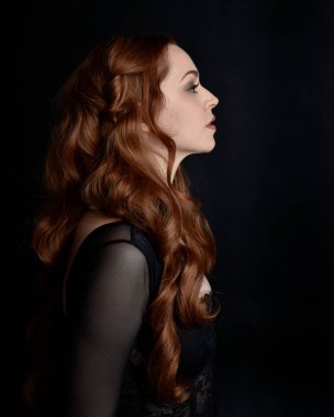 close up portrait of beautiful woman with long red hair wearing sheer corset top. variety of facial expressions,  Isolated on dark studio background with moody silhouette lighting.