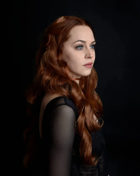 stock image close up portrait of beautiful woman with long red hair wearing sheer corset top. variety of facial expressions,  Isolated on dark studio background with moody silhouette lighting.