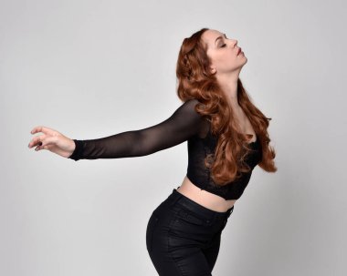 close up portrait of beautiful woman with red hair wearing sheer corset top, leather pants. Posing with gestural hands reaching out. Isolated on white studio background.