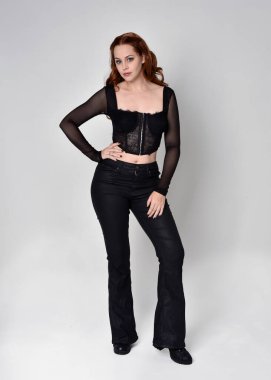 Full length portrait of beautiful woman with long red hair wearing black corset top and leather pants. Standing pose, walking forwards with gestural hands reaching out. Isolated on white studio background. clipart