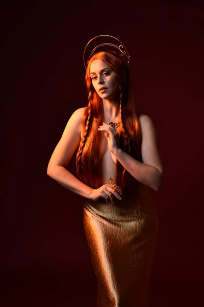 stock image Close up fantasy portrait of beautiful woman model with red hair, goddess silk robes & gold crown.  Posing with gestural hands reaching out, isolated on dark red studio background 