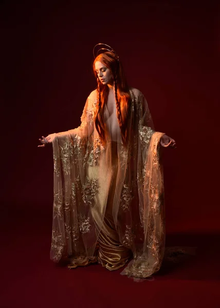 全长的幻想女模特画像 红头发 女神丝绸长袍和金冠 站着摆出姿势 在深红色的工作室背景下伸出孤立的手 — 图库照片
