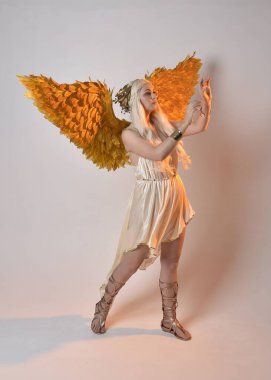 Tüylü melek kanatları olan fantezi tanrıça toga kostümü giyen güzel sarışın kadının tam boy portresi. Atlama pozu, beyaz stüdyo arka planında izole edilmiş..