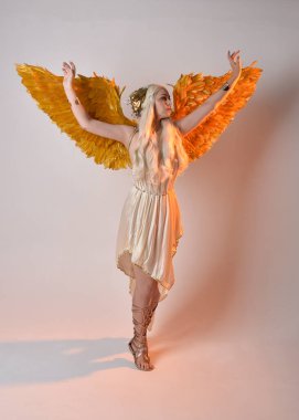 Tüylü melek kanatları olan fantezi tanrıça toga kostümü giyen güzel sarışın kadının tam boy portresi. Atlama pozu, beyaz stüdyo arka planında izole edilmiş..