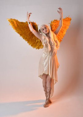Tüylü melek kanatları olan fantezi tanrıça toga kostümü giyen güzel sarışın kadının tam boy portresi. Atlama pozu, beyaz stüdyo arka planında izole edilmiş..