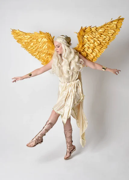 stock image Full length portrait of beautiful blonde woman wearing a fantasy goddess toga costume with feathered angel wings. Jumping pose like flying, isolated on white studio background.