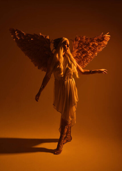 portrait of beautiful blonde woman wearing a fantasy goddess toga costume with  crystal crown.Backlit a glowing isolated studio background with  orange silhouette lighting.