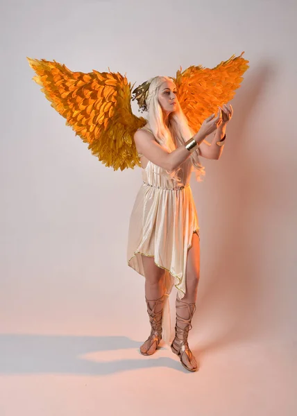 stock image Full length portrait of beautiful blonde woman wearing a fantasy goddess toga costume with feathered angel wings. Jumping pose like flying, isolated on white studio background.