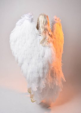 Tüylü melek kanatları olan fantezi tanrıça toga kostümü giyen güzel sarışın kadının tam boy portresi. Atlama pozu, beyaz stüdyo arka planında izole edilmiş..