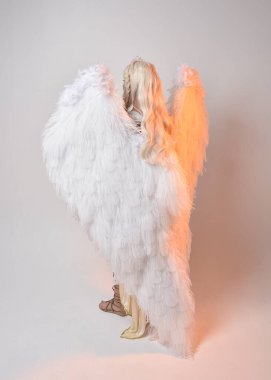 Tüylü melek kanatları olan fantezi tanrıça toga kostümü giyen güzel sarışın kadının tam boy portresi. Atlama pozu, beyaz stüdyo arka planında izole edilmiş..