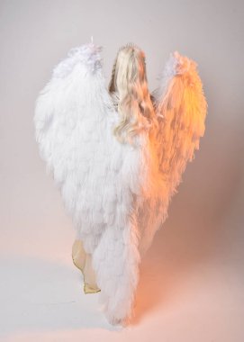 Tüylü melek kanatları olan fantezi tanrıça toga kostümü giyen güzel sarışın kadının tam boy portresi. Atlama pozu, beyaz stüdyo arka planında izole edilmiş..