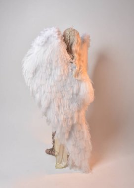 Tüylü melek kanatları olan fantezi tanrıça toga kostümü giyen güzel sarışın kadının tam boy portresi. Atlama pozu, beyaz stüdyo arka planında izole edilmiş..