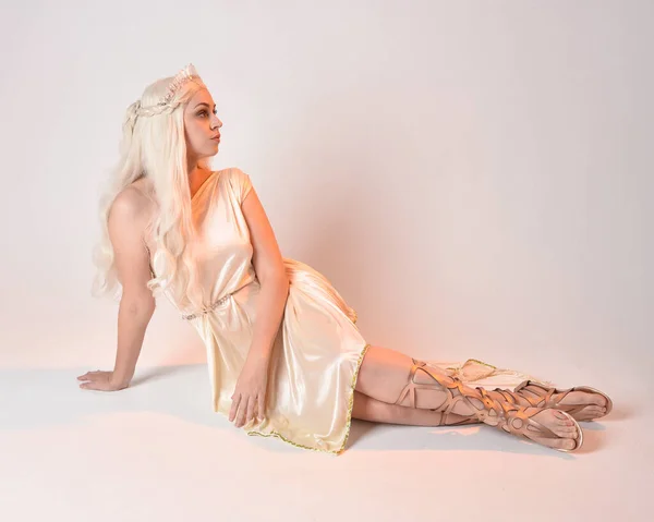 stock image Full length portrait of beautiful blonde woman wearing a fantasy goddess toga costume with  magical crown.Seated pose, sitting on floor. isolated on white studio background.