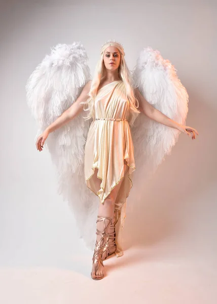 stock image Full length portrait of beautiful blonde woman wearing a fantasy goddess toga costume with feathered angel wings. Jumping pose like flying, isolated on white studio background.