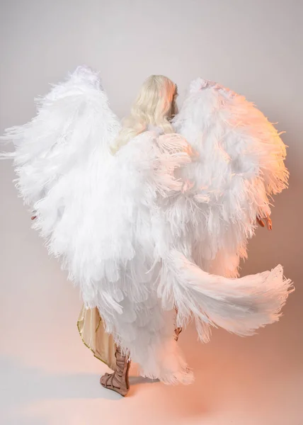 stock image Full length portrait of beautiful blonde woman wearing a fantasy goddess toga costume with feathered angel wings.  Jumping pose like flying, isolated on white studio background.