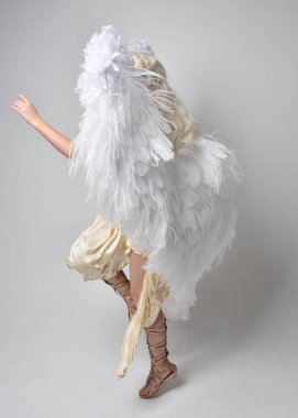 Tüylü melek kanatları olan fantezi tanrıça toga kostümü giyen güzel sarışın kadının tam boy portresi. Atlama pozu, beyaz stüdyo arka planında izole edilmiş..