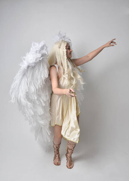 Full length portrait of beautiful blonde woman wearing a fantasy goddess toga costume with feathered angel wings.  Jumping pose like flying, isolated on white studio background.