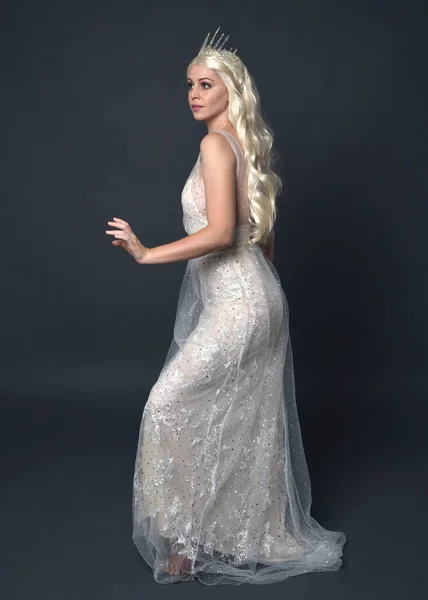 stock image Full length portrait of beautiful women with long blonde hair, wearing fantasy  princess crown and elegant white ball gown, standing pose with hand gesture. Isolated on dark grey studio background.