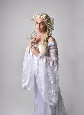 Uzun sarı saçlı, beyaz fantezi prenses elbisesi giyen, beyaz stüdyo arka planında izole edilmiş, güzel bebek nefesi çiçekleri tutan güzel kadınların portresi.