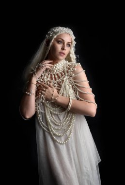 Güzel sarışın mankenin, abartılı bir inci mücevher elbisesi giymiş portresi. Jeolojik kollar uzanıyor, siyah bir stüdyoda izole edilmiş..