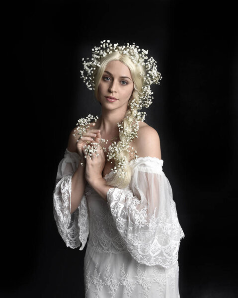 Close up portrait of beautiful women with long blonde hair, wearing white fantasy princess ball gown, holding pretty baby breath flowers, isolated on black studio background