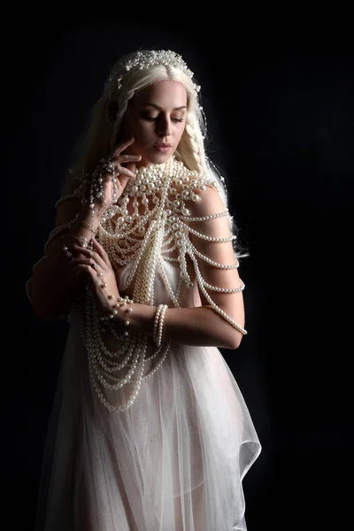 Close up portrait of beautiful blonde female model wearing an extravagant pearl jewelled gown. Gestural arms reaching out,  isolated on a black studio background.