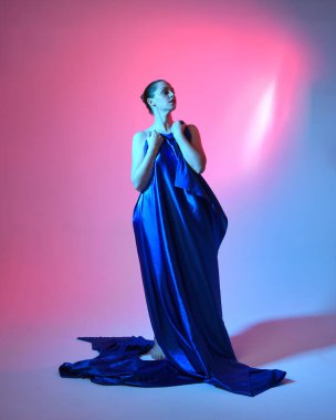 Güzel bir kadın modelin tam boy portresi. Mavi ipek kumaştan zarif bir elbise giyiyor. Stüdyonun arka planında izole edilmiş..