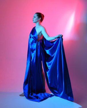 Güzel bir kadın modelin tam boy portresi. Mavi ipek kumaştan zarif bir elbise giyiyor. Stüdyonun arka planında izole edilmiş..