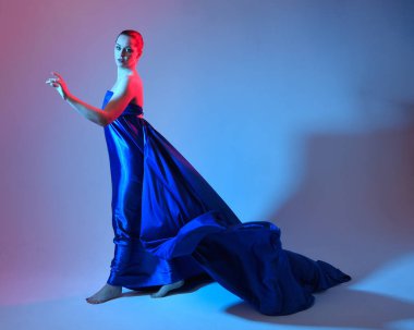 Güzel bir kadın modelin tam boy portresi. Mavi ipek kumaştan zarif bir elbise giyiyor. Stüdyonun arka planında izole edilmiş..