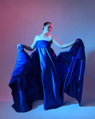 Güzel bir kadın modelin tam boy portresi. Mavi ipek kumaştan zarif bir elbise giyiyor. Stüdyonun arka planında izole edilmiş..