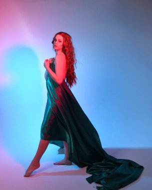 Güzel bir kadın modelin tam boy portresi. Mavi ipek kumaştan zarif bir elbise giyiyor. Stüdyonun arka planında izole edilmiş..