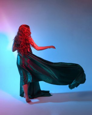 Güzel bir kadın modelin tam boy portresi. Mavi ipek kumaştan zarif bir elbise giyiyor. Stüdyonun arka planında izole edilmiş..