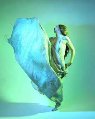 Güzel esmer kadın dansçının uzun bir portresi, ruhani bir elbise giyiyor, akıcı kumaşla dans ediyor. Sinema renkli ışıklandırmayla yeşil stüdyo arka planında izole edilmiş.