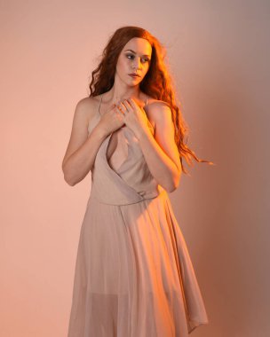 Güzel esmer kadın modelin yakın plan portresi. Altından ışık saçan krem bir elbise giyiyor. El hareketleriyle poz veriyor, stüdyo arka planında izole edilmiş..