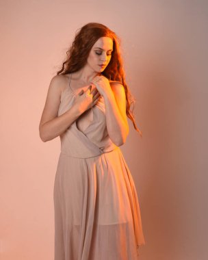 Güzel esmer kadın modelin yakın plan portresi. Altından ışık saçan krem bir elbise giyiyor. El hareketleriyle poz veriyor, stüdyo arka planında izole edilmiş..