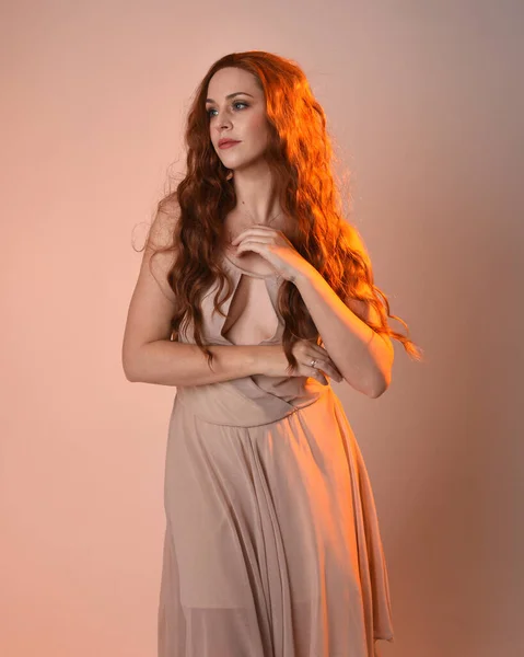 stock image Close up portrait of beautiful brunette  female model wearing a cream dress with golden back light lighting.Gestural arm poses with hands reaching out, isolated on studio background.