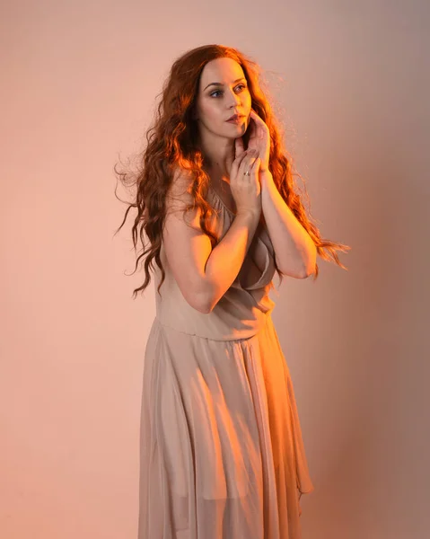 stock image Close up portrait of beautiful brunette  female model wearing a cream dress with golden back light lighting.Gestural arm poses with hands reaching out, isolated on studio background.