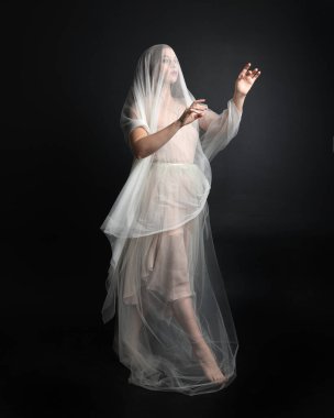 Beyaz cüppeli güzel bir kadının uzun bir portresi. Örtülü, karanlık stüdyo arka planında izole edilmiş beyaz bir elbise giyiyor..