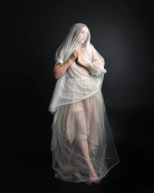 Beyaz cüppeli güzel bir kadının uzun bir portresi. Örtülü, karanlık stüdyo arka planında izole edilmiş beyaz bir elbise giyiyor..