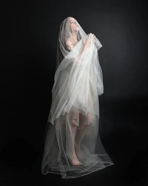 ダークスタジオのバックグラウンドで隔離された幽霊に覆われた生地で白いガウンのドレスを着た美しい女性の完全な長さの肖像画 — ストック写真
