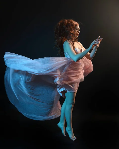 Stock image Full length  portrait of beautiful brunette woman dancer, wearing ethereal gown, dancing with flowing fabric.  isolated on dark studio background with cinematic colourful lighting.