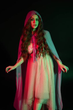 Mor fantezi pelerinli, kollarını uzatarak poz veren güzel esmer kadın portresi. Sinema renkli ışıklandırmayla karanlık stüdyo arka planında izole edilmiş..