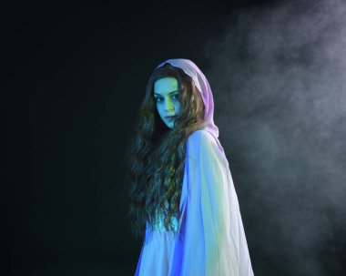 Mor fantezi pelerinli, kollarını uzatarak poz veren güzel esmer kadın portresi. Sinema renkli ışıklandırmayla karanlık stüdyo arka planında izole edilmiş..