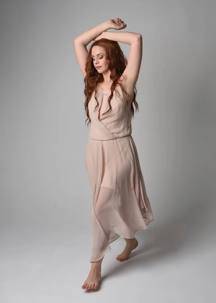 stock image Full length portrait of beautiful  female model with long  brunette hair wearing a creamy pink gown dress. graceful dancing pose, with gestural hands  isolated on white studio background.